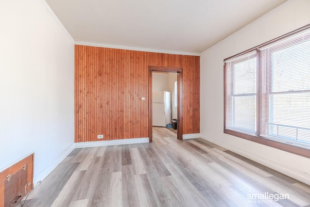 spare room with crown molding, light wood-style floors, baseboards, and wood walls