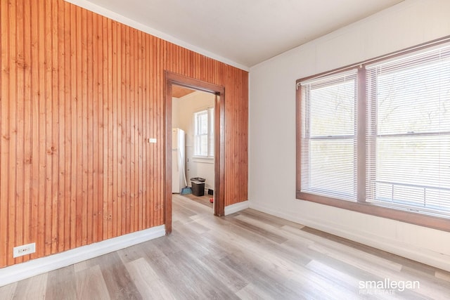 spare room featuring baseboards, wood walls, and light wood finished floors