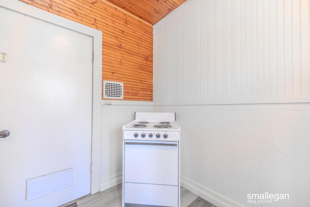 kitchen featuring visible vents, wood walls, light wood-style floors, and white electric range oven