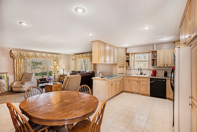 kitchen with light brown cabinetry, freestanding refrigerator, black dishwasher, and a sink