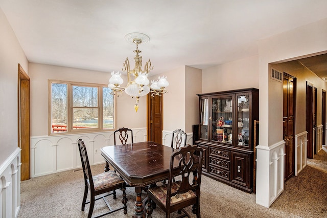 carpeted dining area with visible vents, a chandelier, and wainscoting