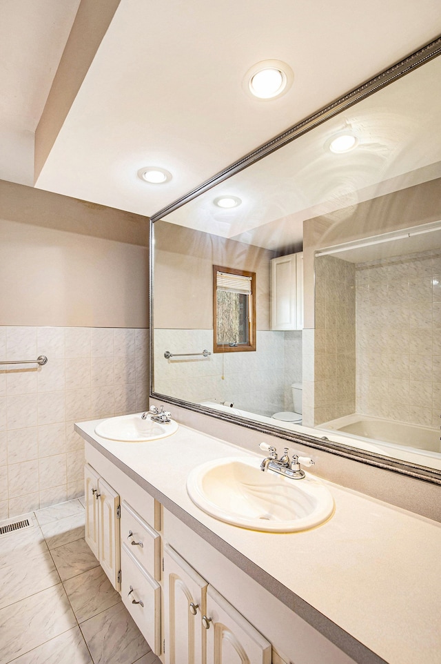 full bathroom with tile walls, toilet, visible vents, and a sink