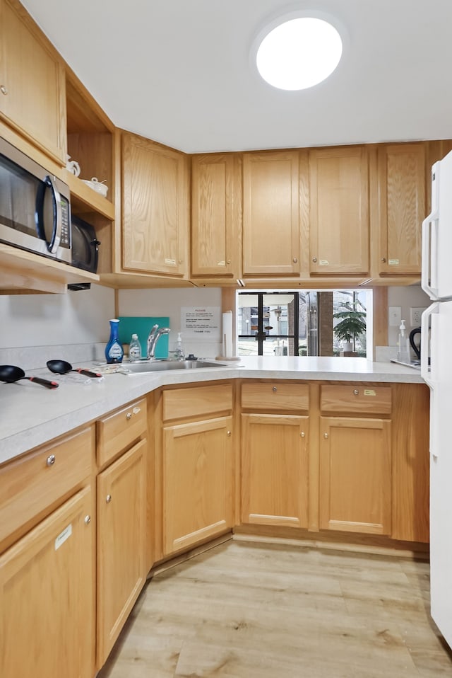 kitchen featuring light wood finished floors, stainless steel microwave, light countertops, and freestanding refrigerator