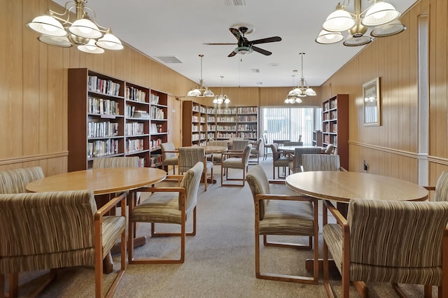 dining space with visible vents, carpet flooring, ceiling fan with notable chandelier, and wood walls