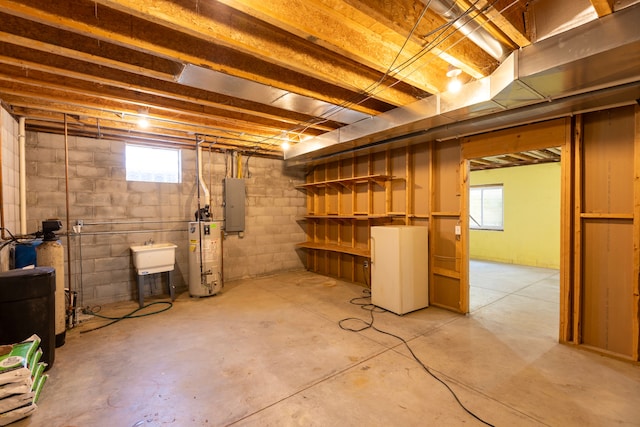 below grade area featuring concrete block wall, electric panel, water heater, and plenty of natural light