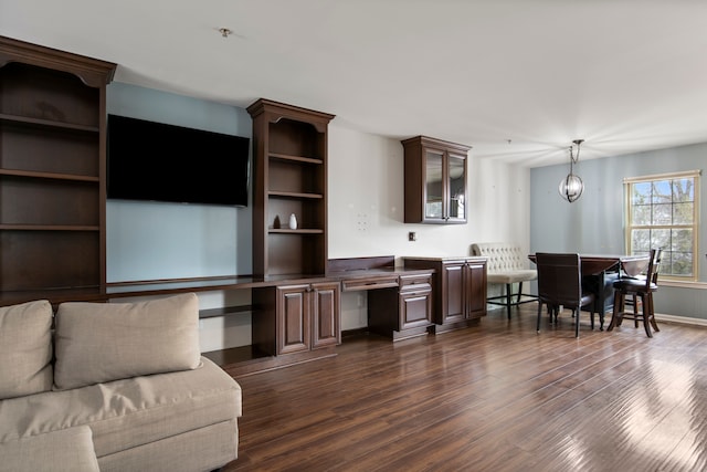 living area with baseboards, a notable chandelier, dark wood-style flooring, and built in study area