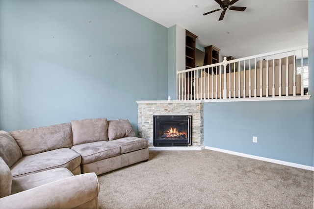 carpeted living area featuring a stone fireplace, baseboards, and ceiling fan