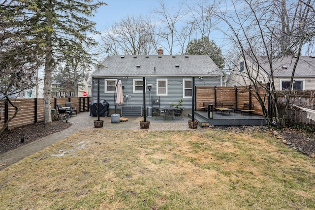 back of house with a shingled roof, a wooden deck, a lawn, a fenced backyard, and a patio area