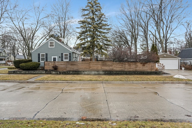 view of property exterior with a detached garage, an outdoor structure, and fence