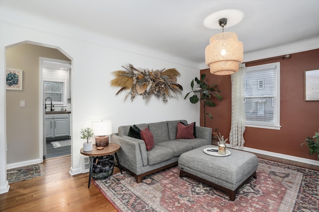 living area with arched walkways, baseboards, and wood finished floors