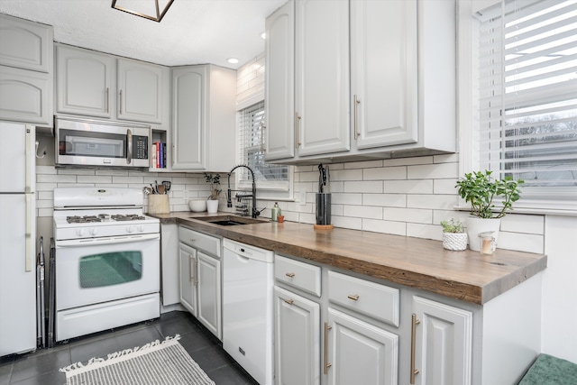 kitchen featuring dark tile patterned flooring, butcher block countertops, a sink, white appliances, and decorative backsplash