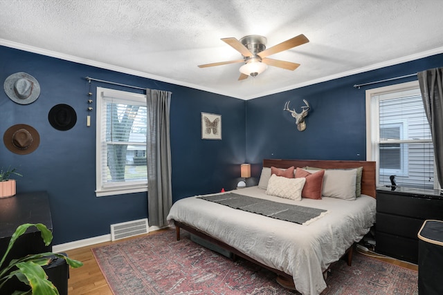 bedroom with visible vents, baseboards, wood finished floors, and crown molding