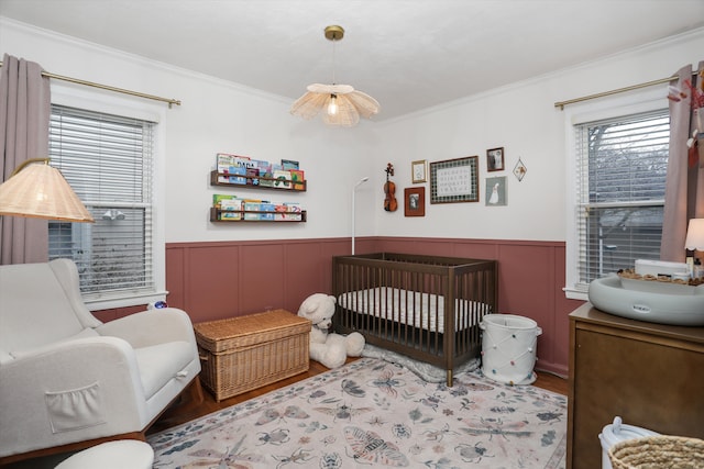 bedroom with a wainscoted wall, multiple windows, a crib, and wood finished floors