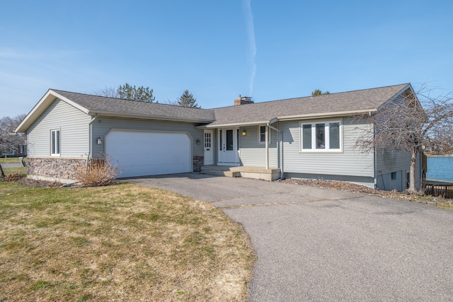 ranch-style house with a front yard, roof with shingles, driveway, an attached garage, and a chimney