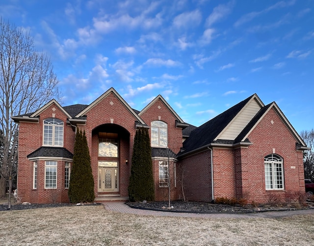 traditional home with a garage, brick siding, and roof with shingles