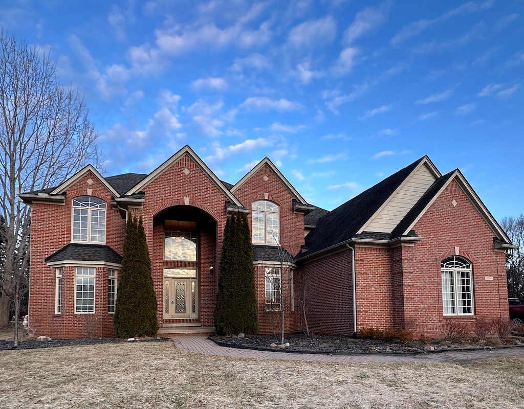 traditional home with a garage, brick siding, and roof with shingles