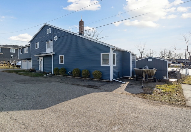 view of front of house with aphalt driveway, fence, a garage, and a chimney