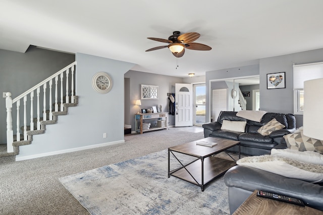 carpeted living area with stairs, a ceiling fan, and baseboards