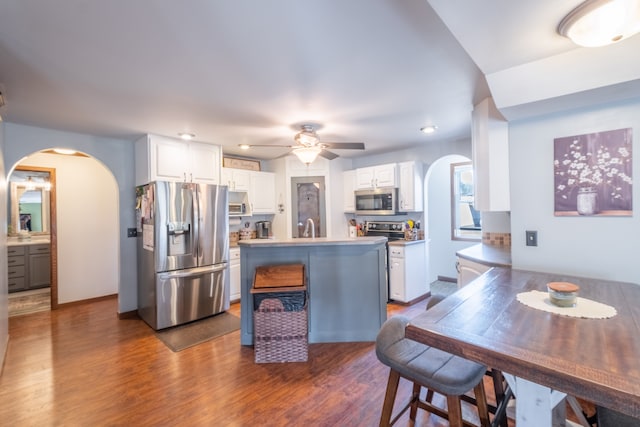 kitchen with dark wood-style floors, arched walkways, white cabinets, stainless steel appliances, and a sink