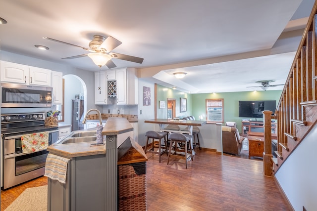 kitchen with a ceiling fan, a sink, open floor plan, appliances with stainless steel finishes, and white cabinets