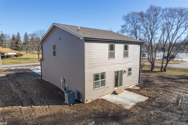 rear view of property featuring entry steps, central AC unit, and a shingled roof