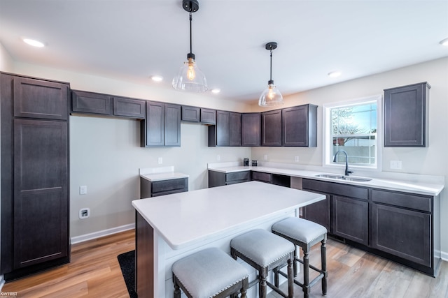 kitchen with a breakfast bar, a sink, decorative light fixtures, a center island, and light wood-style floors