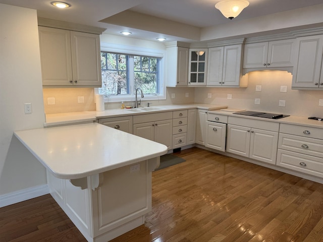 kitchen with a kitchen bar, a sink, a peninsula, black electric cooktop, and dark wood-style flooring