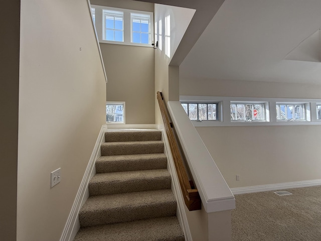 staircase with visible vents, baseboards, carpet, and a high ceiling