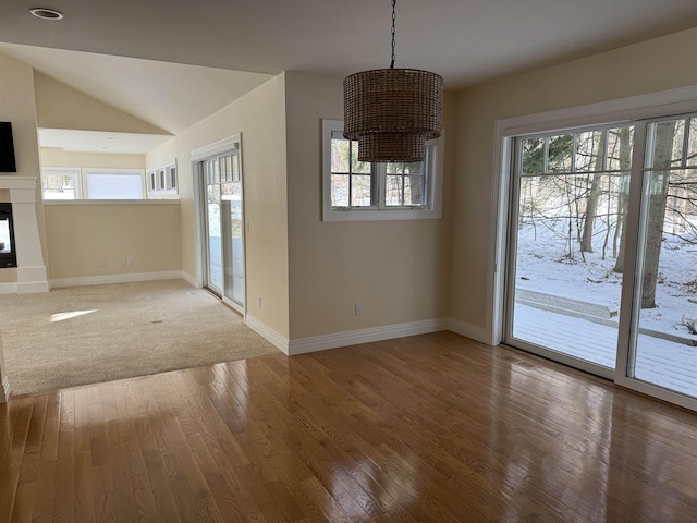 unfurnished dining area featuring a glass covered fireplace, baseboards, lofted ceiling, and wood-type flooring