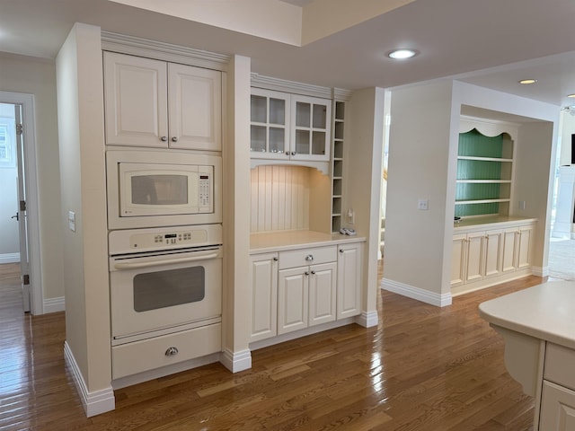 kitchen with baseboards, white appliances, wood finished floors, and light countertops