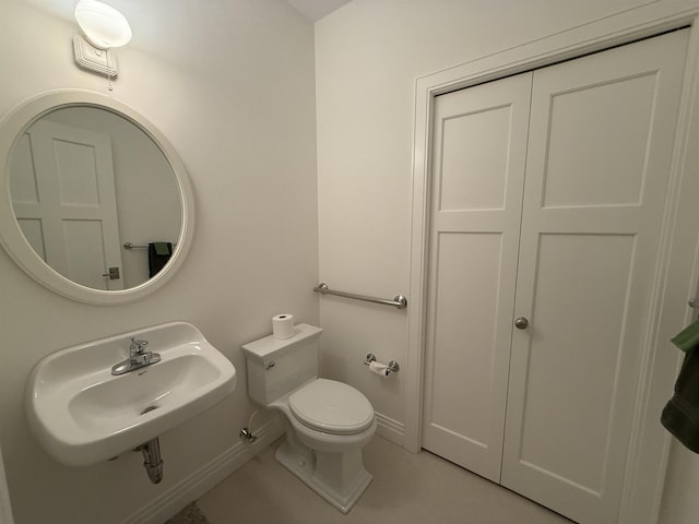 half bath with tile patterned flooring, toilet, baseboards, and a sink