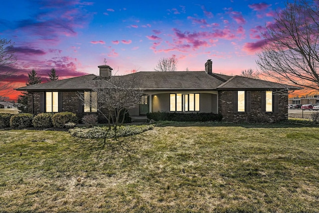 view of front of house with a yard, fence, brick siding, and a chimney