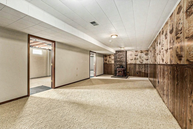 below grade area featuring a wainscoted wall, visible vents, carpet floors, wooden walls, and a wood stove