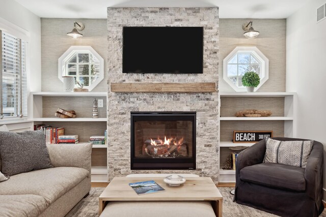 living room featuring visible vents, a stone fireplace, and wood finished floors