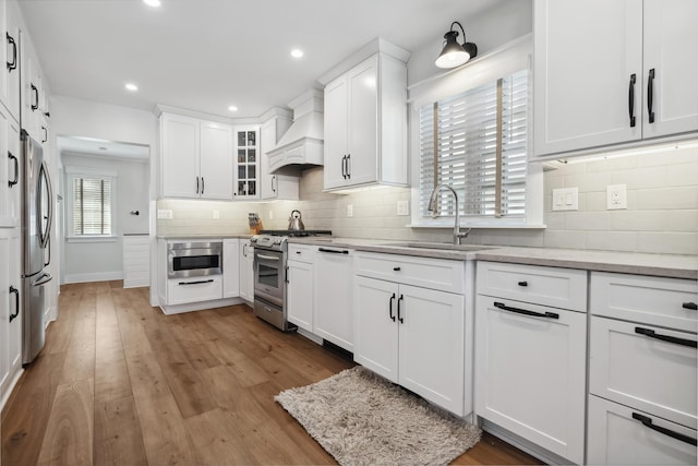 kitchen featuring a sink, premium range hood, white cabinetry, and stainless steel appliances