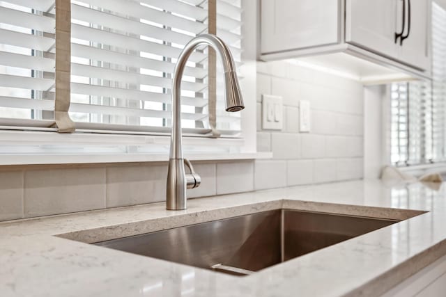 interior details featuring tasteful backsplash, light stone countertops, and a sink