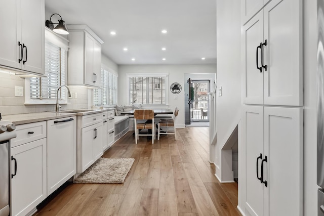 kitchen with decorative backsplash, light wood-style flooring, white dishwasher, white cabinetry, and a sink