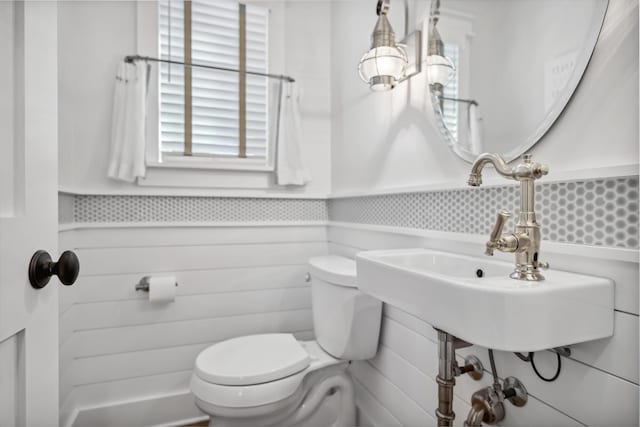 half bath with wainscoting, toilet, and a sink