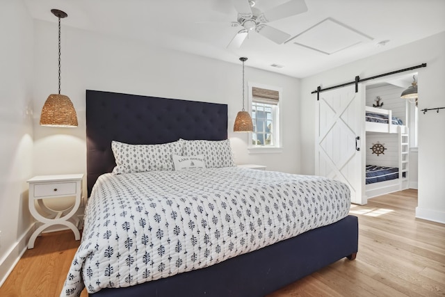 bedroom featuring visible vents, light wood-style flooring, a ceiling fan, a barn door, and baseboards