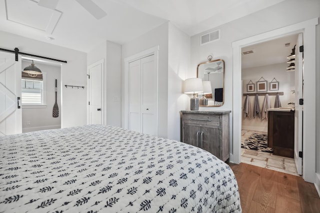 bedroom featuring visible vents, wood finished floors, connected bathroom, a barn door, and a closet