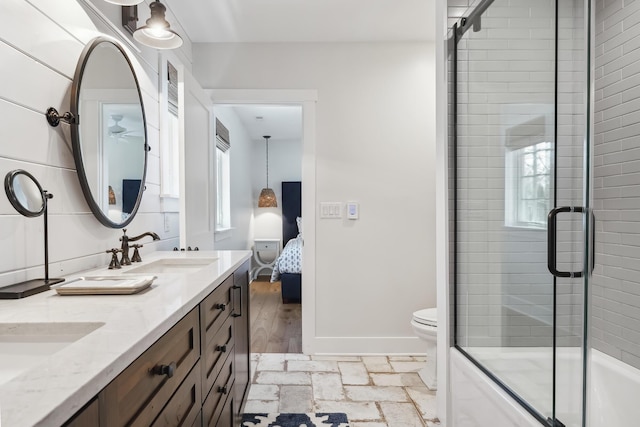 full bath with stone tile floors, baseboards, a sink, ensuite bathroom, and toilet