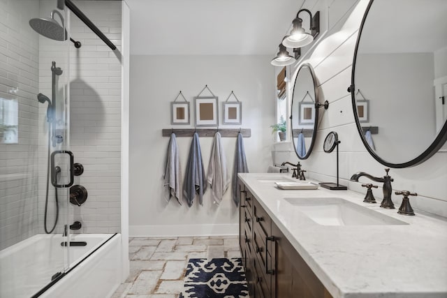 bathroom featuring stone tile floors, baseboards, shower / bath combination with glass door, and a sink