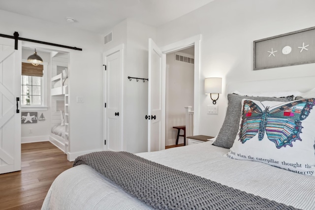 bedroom with visible vents, baseboards, a barn door, and wood finished floors