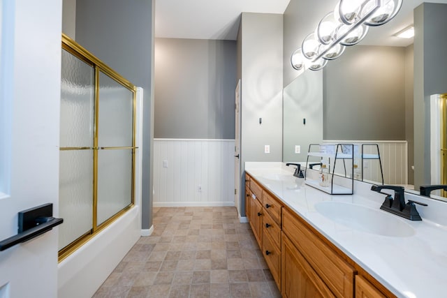 bathroom featuring double vanity, a wainscoted wall, combined bath / shower with glass door, and a sink