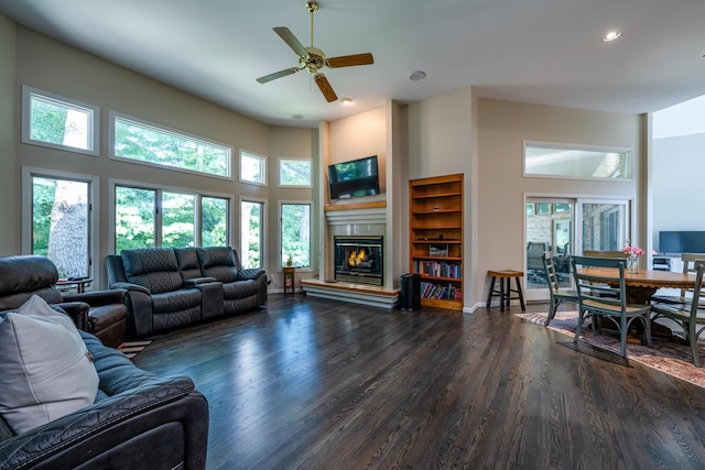 living room with wood finished floors, a glass covered fireplace, recessed lighting, a high ceiling, and ceiling fan