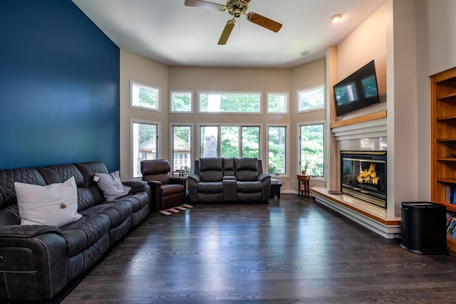 living area with a ceiling fan, a high ceiling, a glass covered fireplace, and dark wood-style flooring