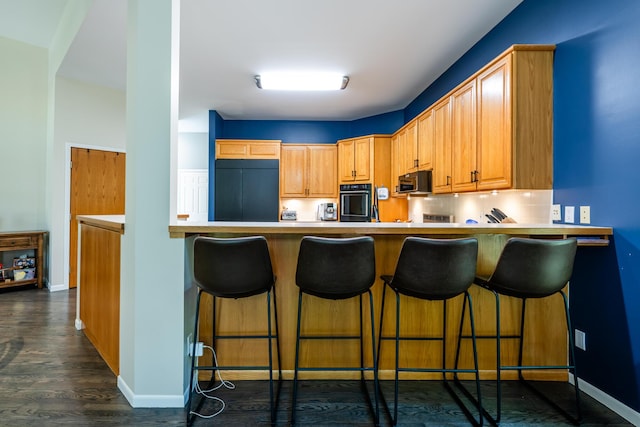 kitchen with black oven, light countertops, built in fridge, a peninsula, and dark wood-style flooring