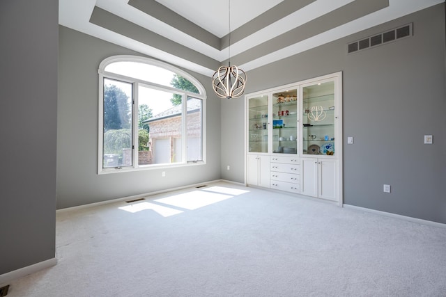 carpeted spare room with visible vents, baseboards, and an inviting chandelier