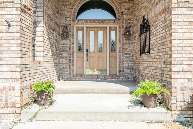 view of exterior entry with a porch and brick siding