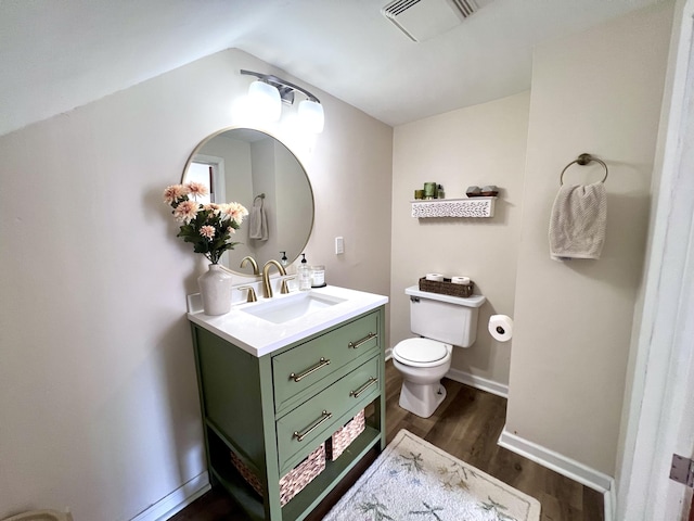 half bath featuring vanity, wood finished floors, visible vents, baseboards, and toilet